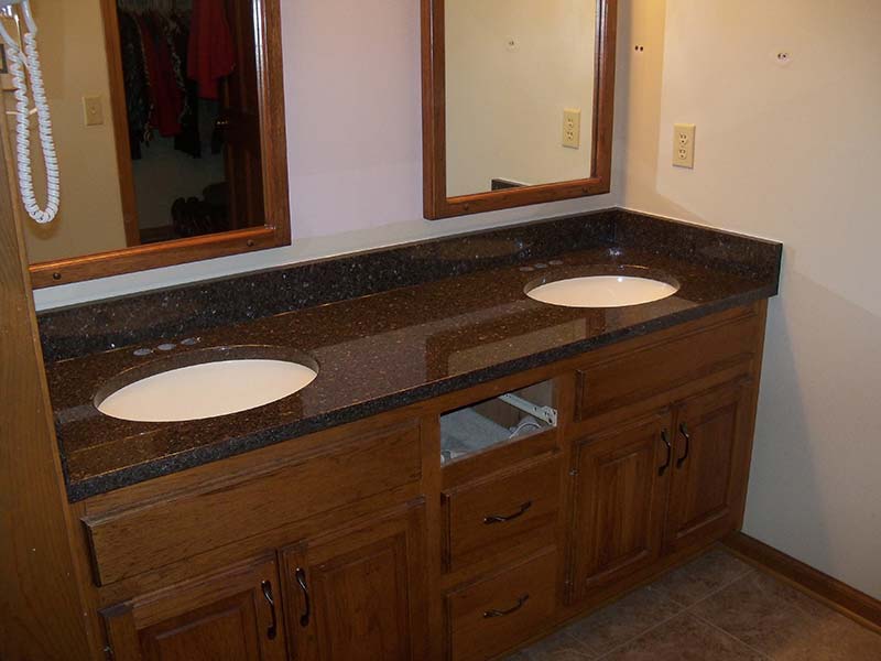 Brown Pearl aka Imperial Coffee Granite bathroom counter with double sinks over medium wood toned cabinets.