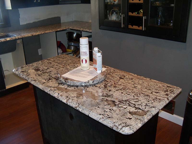Lennon Granite sideboard cabinet coordinates with the Lennon Granite kitchen counters surrounded by dark wood cabinets.