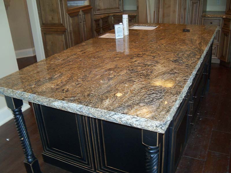 Stormy Night Granite over a dark kitchen island surrounded by medium wood toned cabinets.